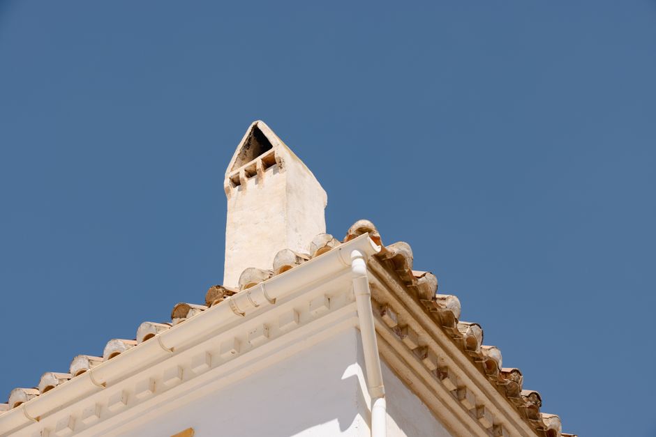 Close-up of a traditional Spanish roof and chimney against a clear blue sky.